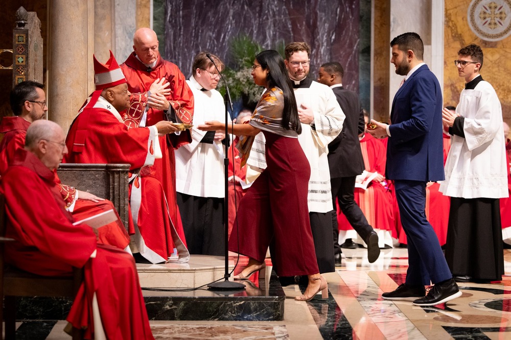 Wilton seated and vested accepts offering from young woman.