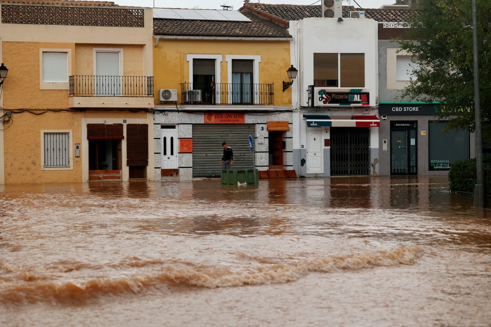 Flood aftermath, Valencia, Spain, Oct. 30, 2024. Street runs with a river of brown water past low, attached buildings.