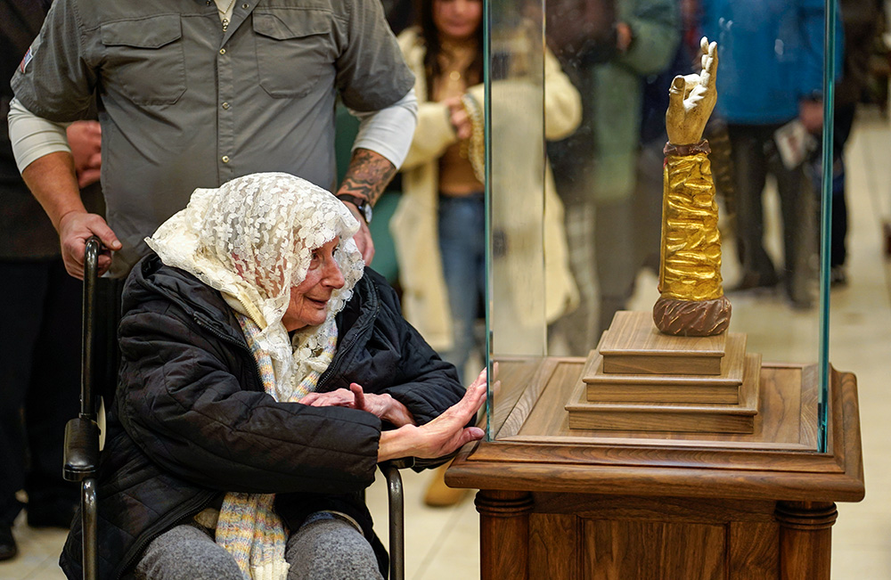 A woman presses her hand against a glass case protecting a reliquary containing a bone from the arm of St. Jude the Apostle at St. Jude Church in Mastic Beach, N.Y., Nov. 27, 2023. The relic, which arrived in Chicago from Italy in September,was on a nine-month tour of the U.S. (OSV News/Gregory A. Shemitz)