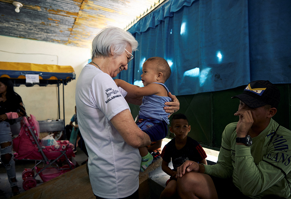 La hermana scalabriniana Rosita Milesi, galardonada con el Premio Nansen 2024 para Refugiados de Acnur, sostiene a Alexander Solis y saluda a refugiados y migrantes venezolanos mientras esperan para recoger kits de higiene y nutrición donados en la Casa de Acolhida Sao Jose, un refugio temporal para refugiados y migrantes en Pacaraima, Brasil, el 24 de agosto. (Foto: Acnur/Marina Calderón/Reuters)