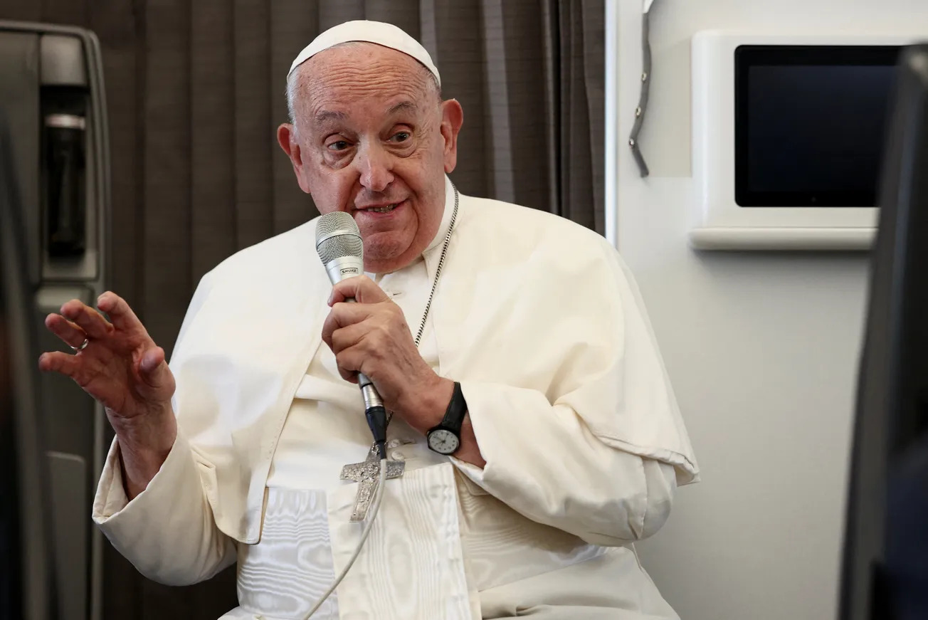 Francis sits, speaking into microphone and smiling. 