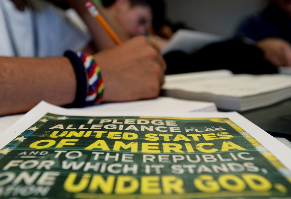 A copy of the Pledge of Allegiance rests on a desk next to an immigrant in a writing class at the U.S. government's holding center for migrant children in Carrizo Springs, Texas, July 9, 2019. (CNS/Eric Gay, pool via Reuters)