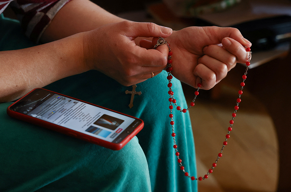 Una mujer ucraniana que huyó de la invasión rusa a Ucrania reza el rosario usando su teléfono móvil en Lubaczow, Polonia, el 21 de marzo de 2022. (Foto: OSV News/Reuters/Kacper Pempel)