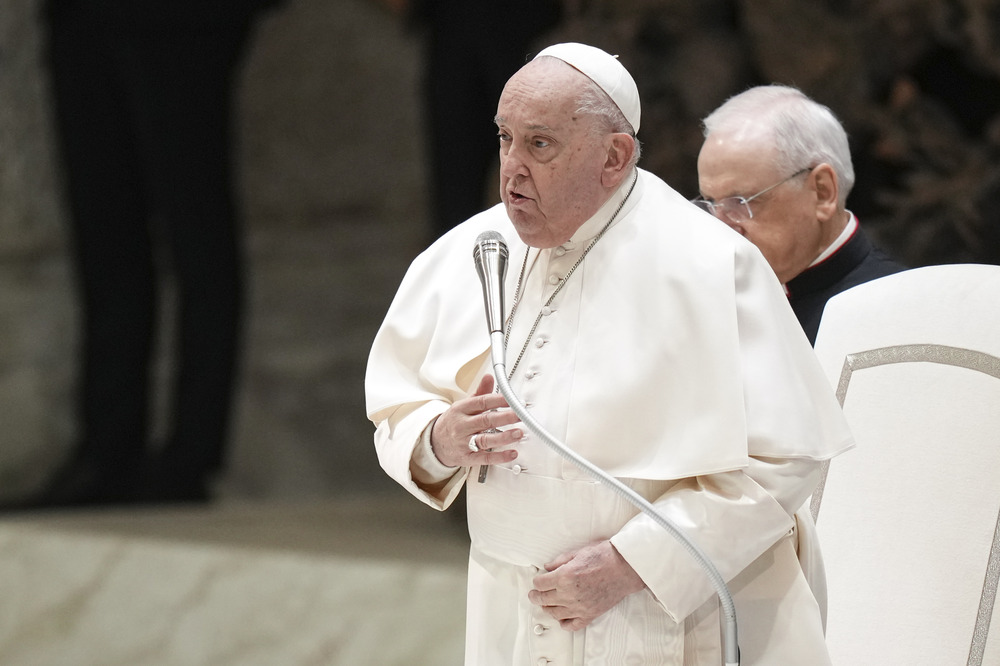 Pope Francis, general audience on Wednesday Jan. 22, 2024 in the Vatican; Prays for Los Angeles wildfires. The pope stands speaking into microphone with hand to chest.