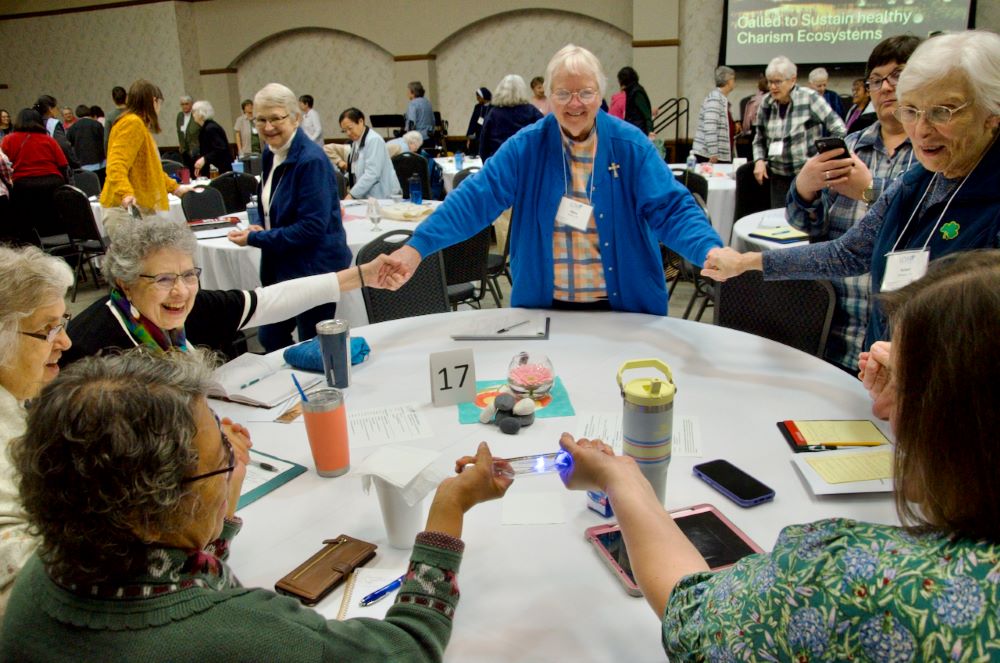 Women stand around table and hold hands. 