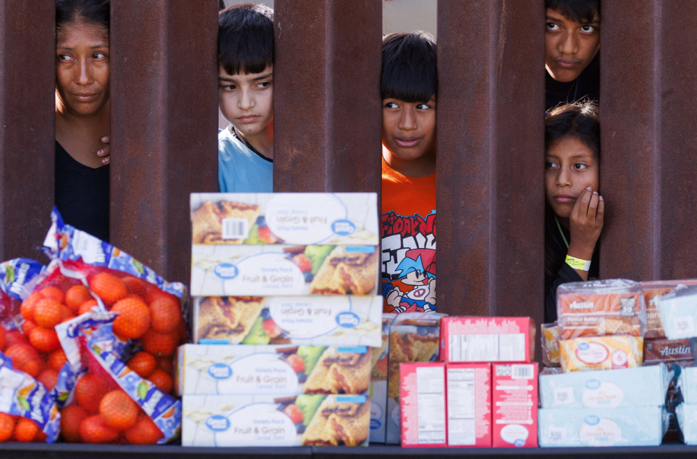 Migrants look through the border fence Sept. 12, 2023, toward food brought by aid workers after gathering between the primary and secondary border fences at the U.S.-Mexico border to wait for processing by U.S immigration officials in San Diego. (OSV News/Reuters/Mike Blake)