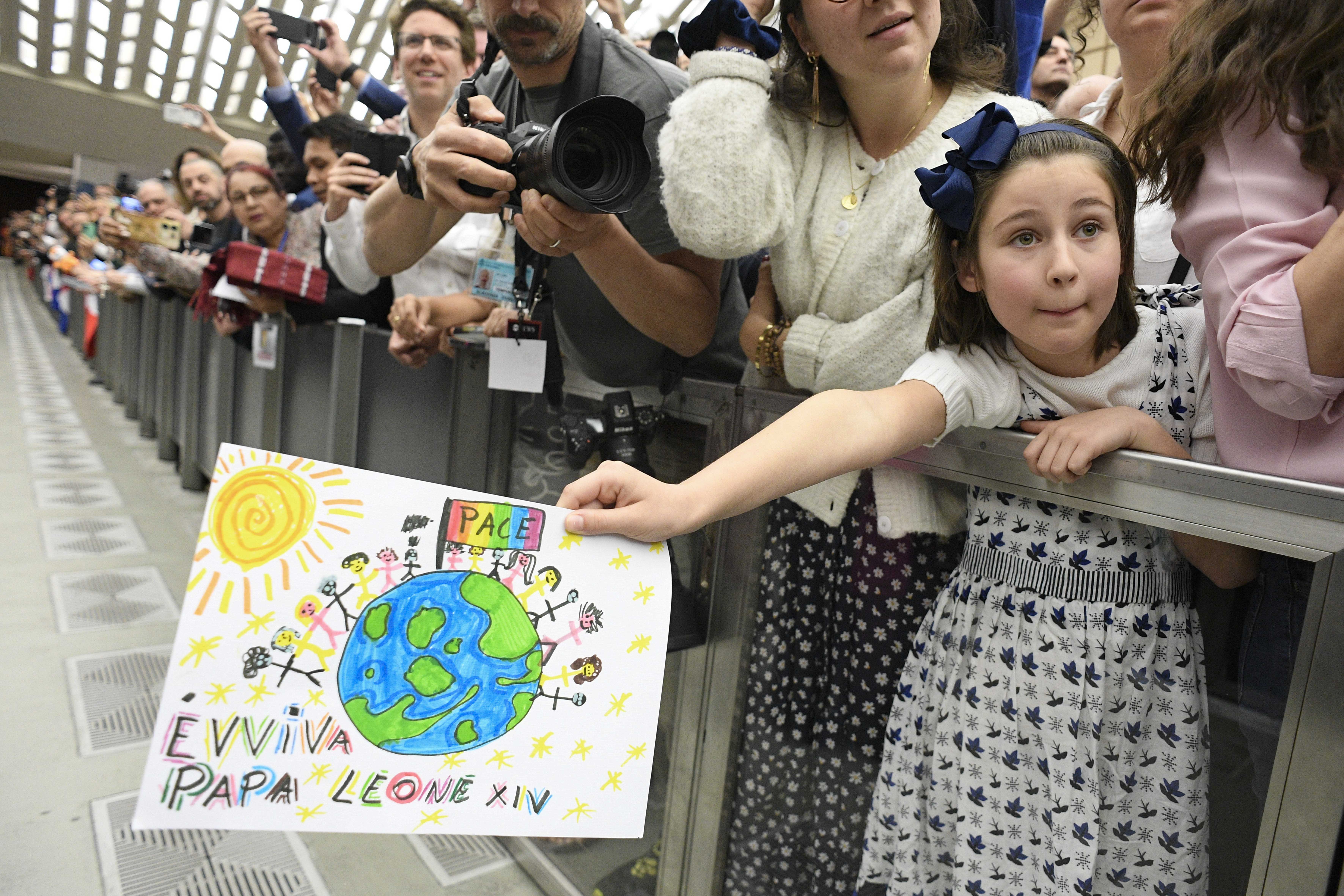 A girl holds out a drawing she made for Pope Leo XIV, hoping that he will accept it after his meeting with members of the media May 12, 2025, in the Paul VI Audience Hall at the Vatican. 