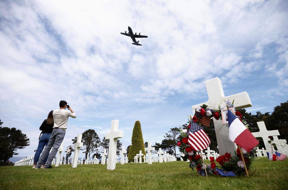 A C-130 aircraft flies over the World War II Normandy American Cemetery and Memorial.  