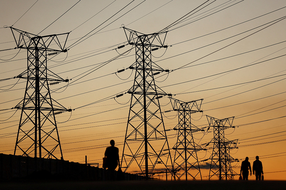 People in Soweto, South Africa, walk past electricity pylons July 3, 2022, during frequent power outages because of aging coal-fired plants. (CNS/Reuters/Siphiwe Sibeko)