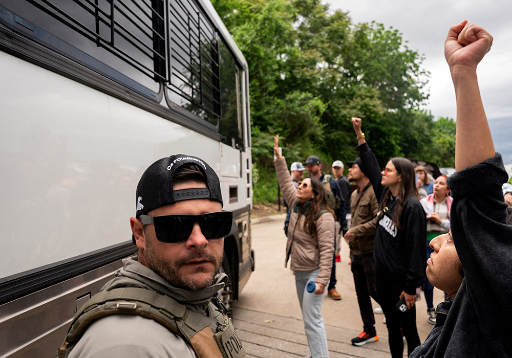 An Immigration and Customs Enforcement officer looks on as a bus transporting detained people leaves the Department of Homeland Security field office in Nashville, where multiple immigrant rights groups gathered to protest what they believed to be a multi-agency operation to detain-noncitizens overnight in Nashville, Tennessee, on May 4, 2025. (OSV News/Reuters/Seth Herald)