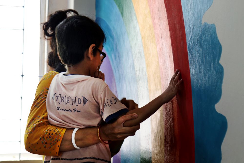 Volunteer with child and rainbow painted on wall.