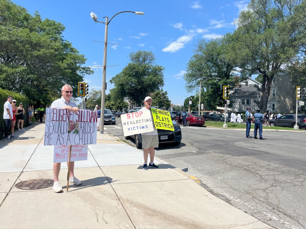 2 people hold protest signs referring to clergy sex abuse. 2 people hold protest signs referring to clergy sex abuse.