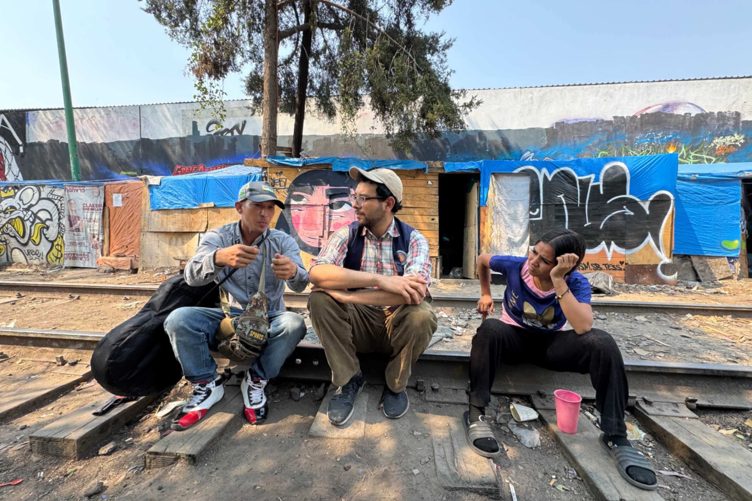 Jesús Ricardo Rojas Romero, de Venezuela, platica con Mario Monroy, y Yesenia, también de Venezuela, el 1 de abril de 2025 en un campamento de migrantes en Ciudad de México. Monroy, coordinador de integración local para Cafemin —un albergue para mujeres y familias en Ciudad de México— dice que en su trabajo ve la cara más cruenta de la sociedad: el maltrato a los migrantes. (Foto: GSR/ Rhina Guidos) 