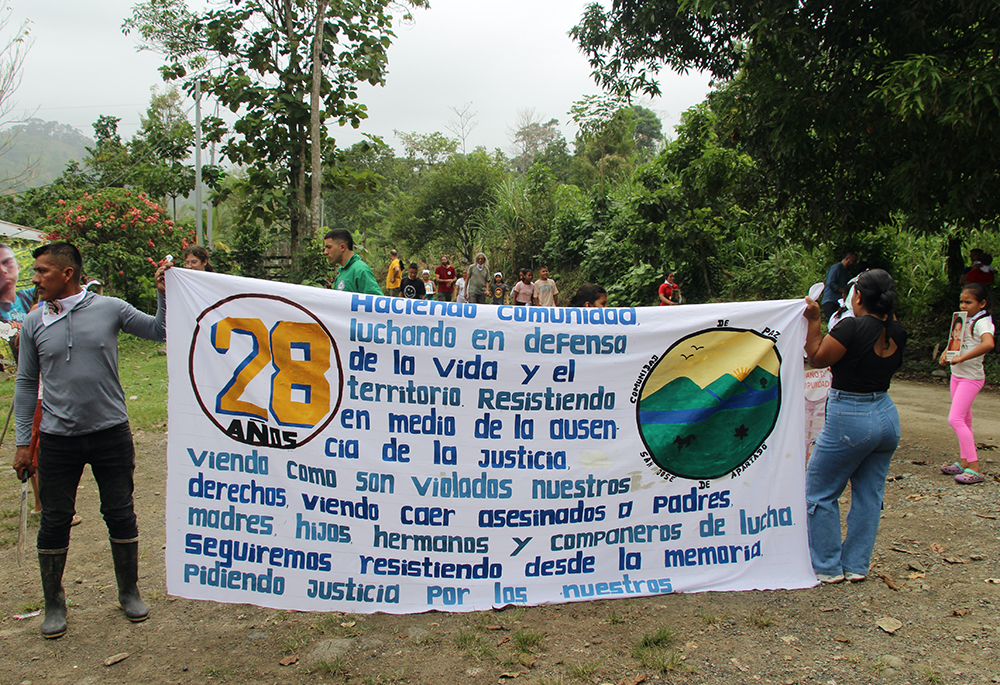Miembros de la comunidad sostienen un cartel durante su procesión hacia las tumbas de los miembros asesinados en 2024.  (Foto: Tracy L. Barnett)