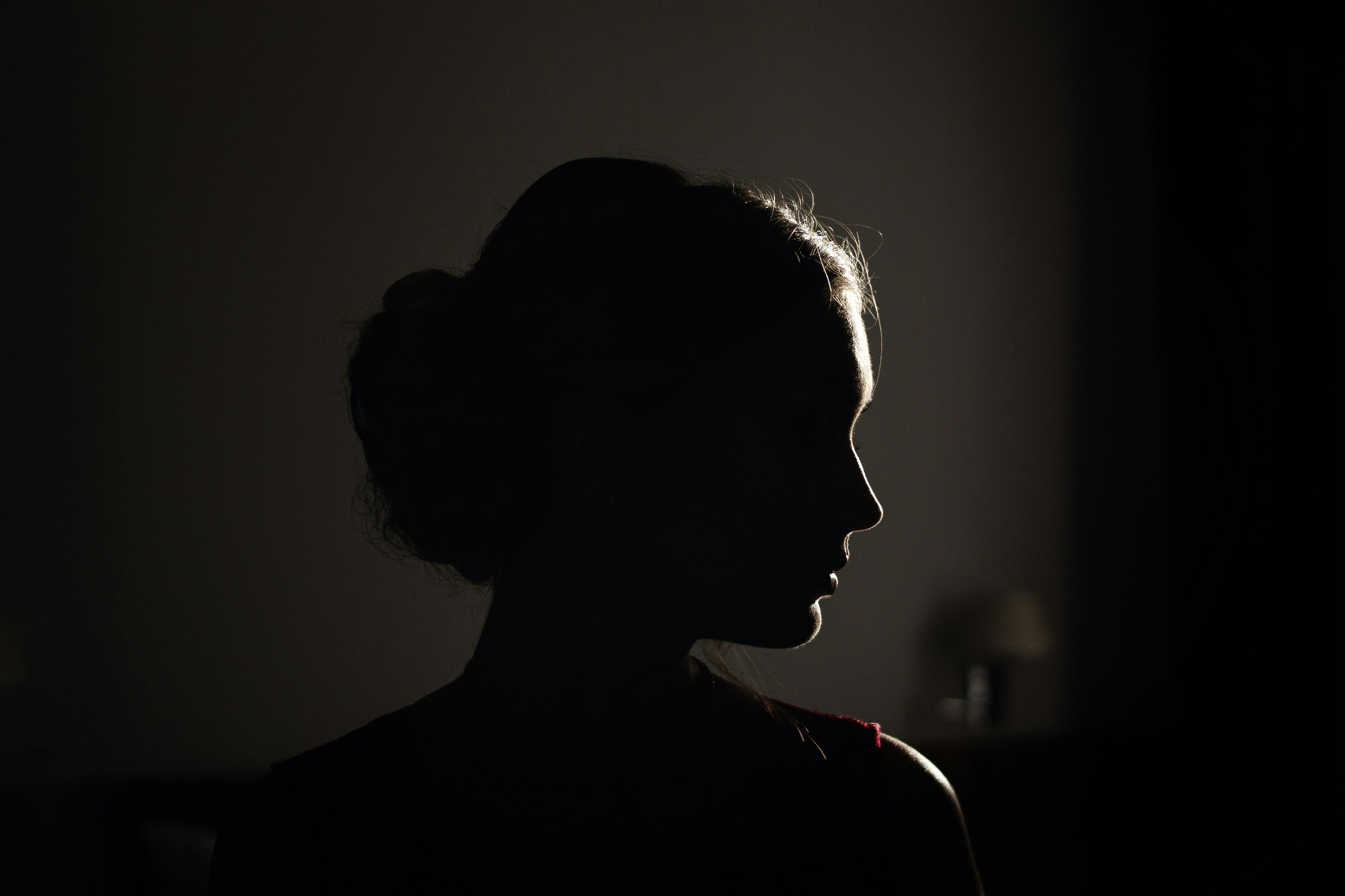 A dark photo illustration shows a close-up profile of a woman in shadow, with light shining just behind her right side. (Unsplash/Andrey Zvyagintsev)