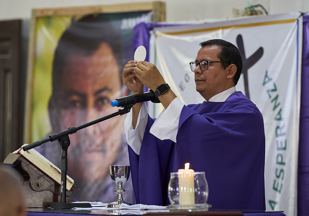 Jesuit Fr. Carlos Orellana preaches during Mass in the San Isidro Labrador Catholic Church in Tocoa, Honduras, on March 23, 2025. Behind him is a portrait of Juan López, a Catholic delegate of the word who was assassinated in Tocoa on Sept. 14, 2024. (NCR photo/Paul Jeffrey)