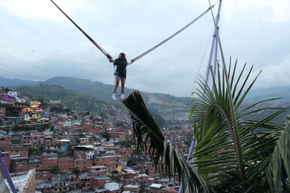 Una turista salta en una cama elástica con arnés en una franja tipo malecón en la cima de la colina en Medellín, Colombia. Al fondo se encuentra La Escombrera, un enorme relleno sanitario industrial de la ciudad donde organizaciones de derechos humanos y familias aseguran que hay cientos de cuerpos enterrados. En diciembre, peritos forenses hallaron allí los restos de cuatro cuerpos. (Foto: Tracy L. Barnett)