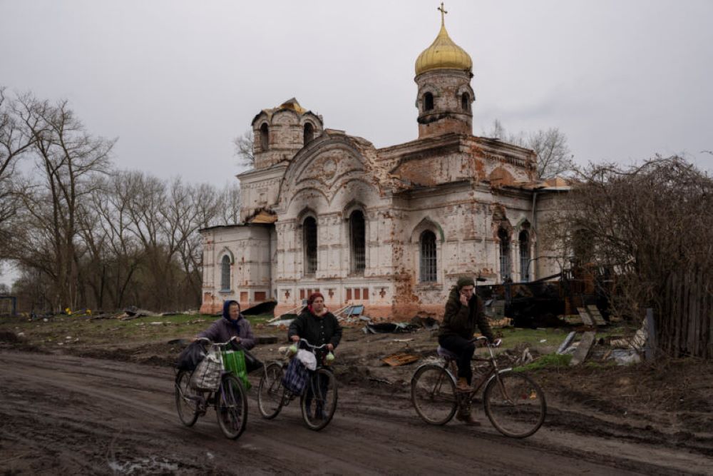 Residents walk with their bicycles in front of a damaged church. Residents walk with their bicycles in front of a damaged church.