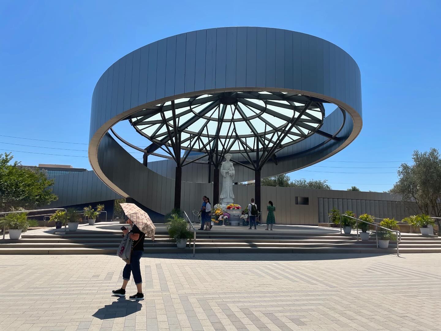 A woman shaded by an umbrella walks past the shrine in June 2025. 