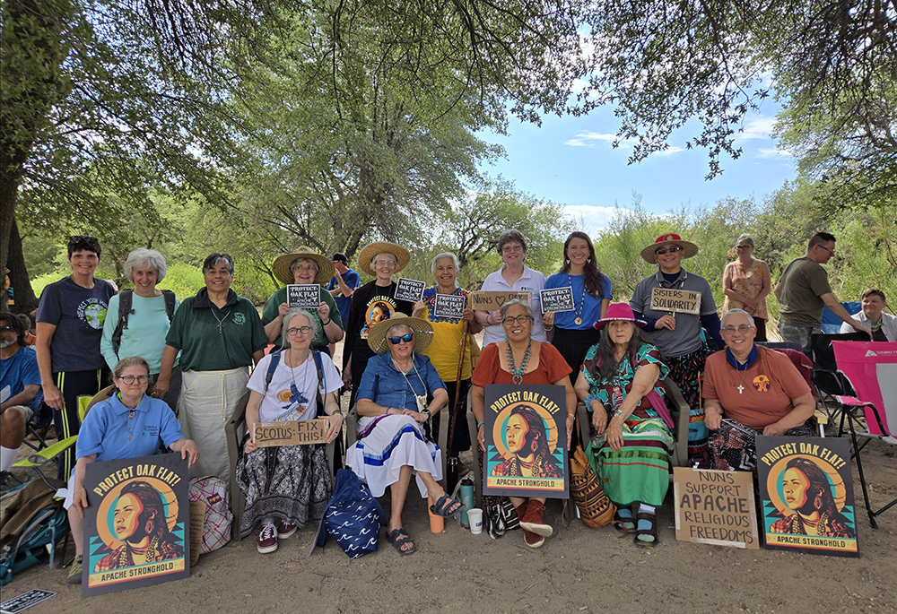 Under a tree canopy at Oak Flat, members of the Land Justice Futures delegation hold signs in support of Apache religious freedoms and rights. (Courtesy of Land Justice Futures)