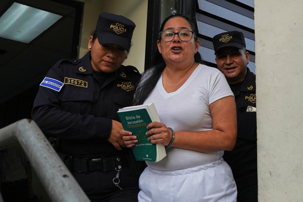 La abogada de derechos humanos Ruth Eleonora López, esposada, sostiene una Biblia mientras la policía la escolta al salir de su audiencia judicial en San Salvador, El Salvador, el 4 de junio de 2025. (Foto: AP/Salvador Meléndez)