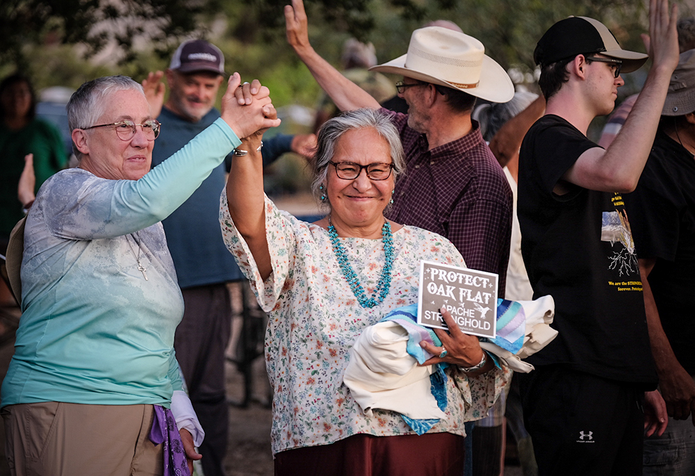 Diné elder and adviser to the delegation, Pat McCabe, center, and Providence Sr. Barbara Battista grab hands in celebration and solidarity at the gathering, held July 18-20, in defense of Oak Flat in southeastern Arizona's Tonto National Forest. (Courtesy of Steve Pavey)