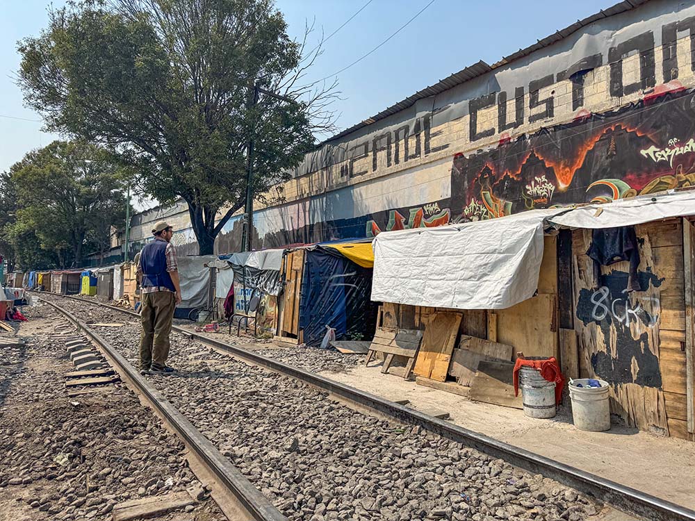 Mario Monroy, outreach coordinator at CAFEMIN, a shelter for women and families run by Josephine sisters in Mexico City, greets a woman living inside a shack April 1, 2025, at a camp migrants have set up near train tracks. Monroy and other workers from the nearby shelter check in on their welfare and provide information as well training for temporary work for migrants. (GSR photo/Rhina Guidos)