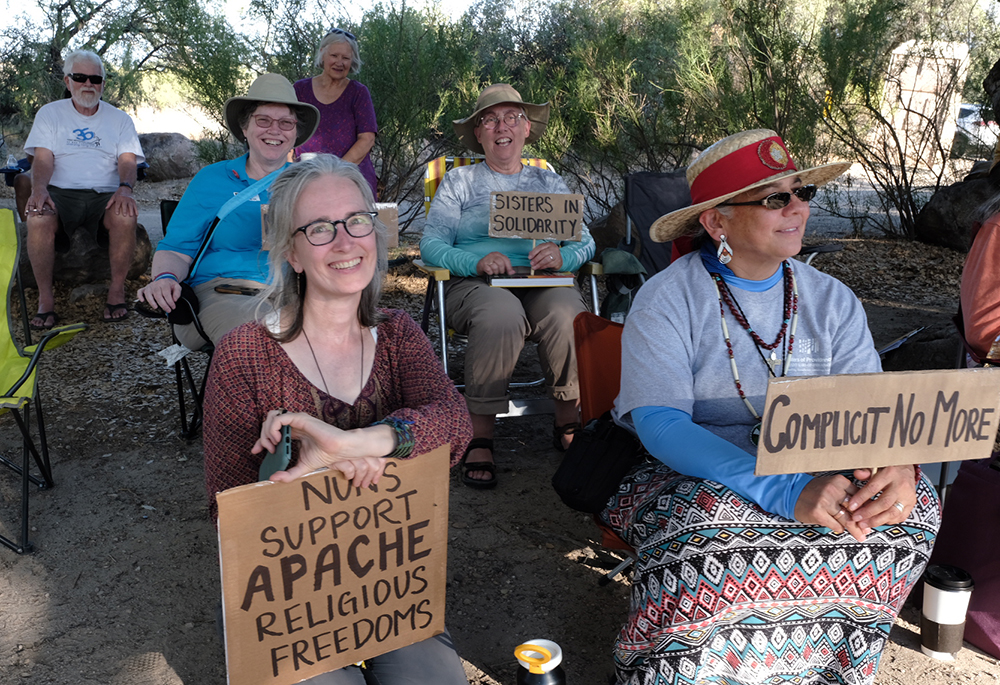 Sisters sit under the oak trees at Oak Flat with signs in support of the community organization Apache Stronghold. In front, left to right: Sr. Kristin Peters of the Franciscan Sisters of Perpetual Adoration and Sr. Joni Luna of the Sisters of Providence. In the back are Dominican Sr. Susan Leslie and Sr. Barbara Battista, Sisters of Providence. (Courtesy of Steve Pavey)