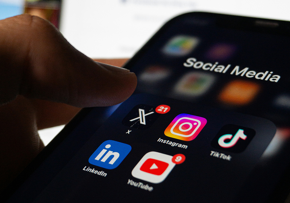 A close-up photo illustration shows a user hovering with their thumb over social media app icons displayed on a smartphone. (Unsplash/Berke Citak)