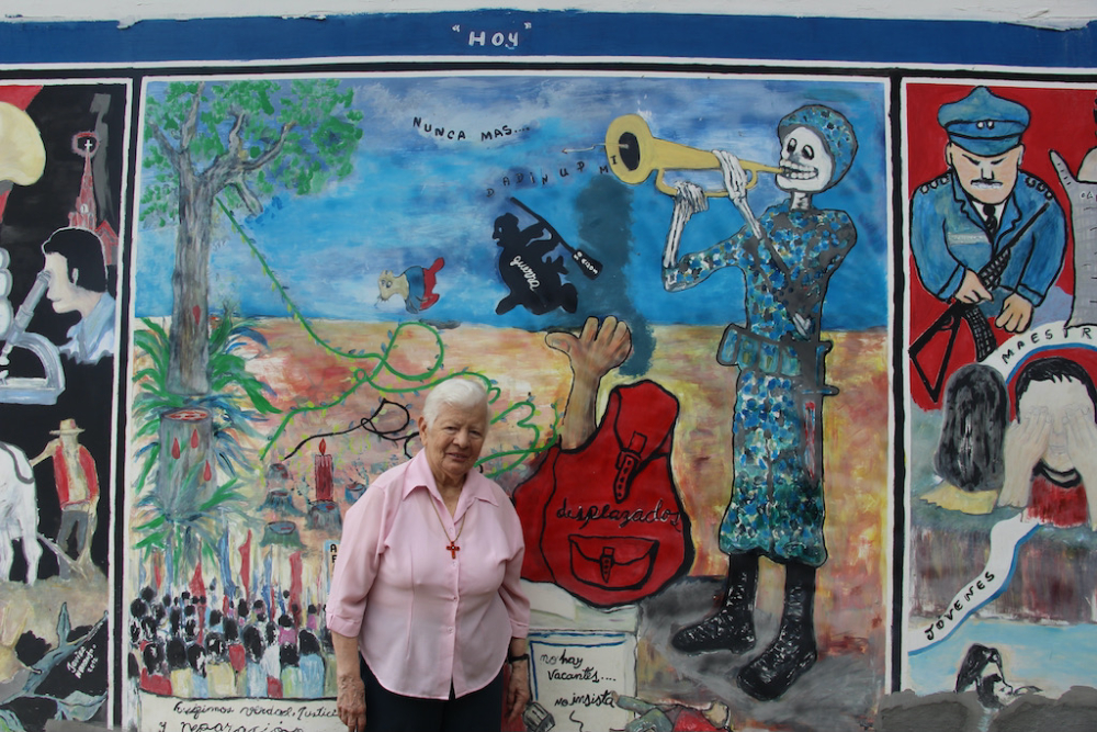 La Hna. Maritze Trigos Torres explica la "triptica", un mural que lleva a los espectadores a través del sangriento pasado de Trujillo (a la derecha), hasta su presente marcado por las luchas por la justicia (en el centro), y su futuro esperanzador, lleno de abundancia, educación, buena salud y buena fortuna. (Foto: Tracy L. Barnett)