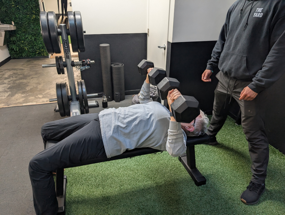 Sr. Pat Farrell lifts two 30-pound dumbbells while Jake Levine, a trainer at The Yard gym, spots her.