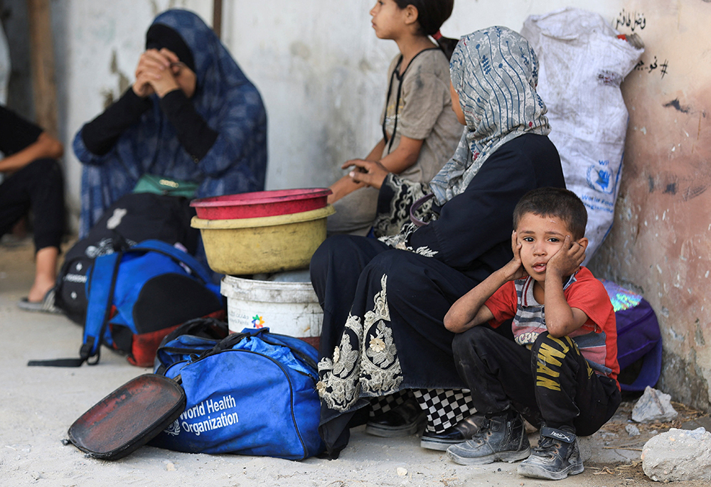 A child looks on as a displaced Palestinian family sits on the ground outside Al-Ahli Arab Hospital in Gaza City, Aug. 26, 2025, after fleeing deadly Israeli strikes. (OSV News/Reuters/Dawoud Abu Alkas)