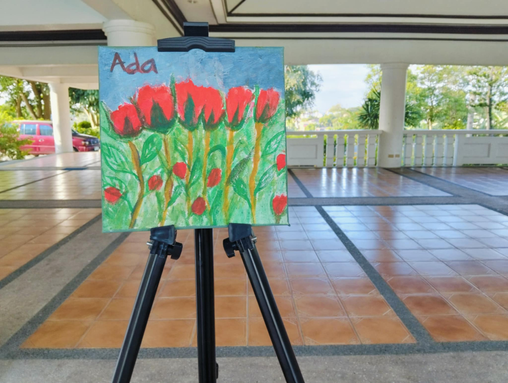 A photo of a painting one of the shelter's residents made. A close up of bunch of six red tulips in a green field on a clear day, signed "Ada."