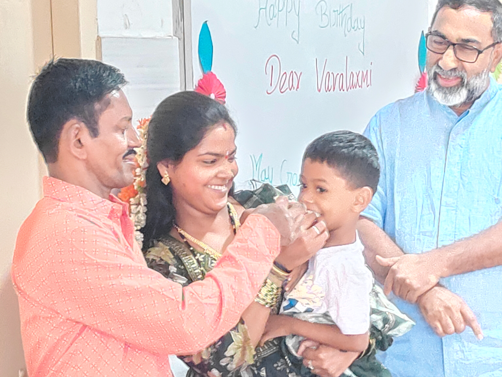 Varalakshmi, a resident of Sumanahalli celebrates her birthday with her husband (left) and daughter. Claretian Fr. George Kannanthanam (right) is also present. (Thomas Scaria)
