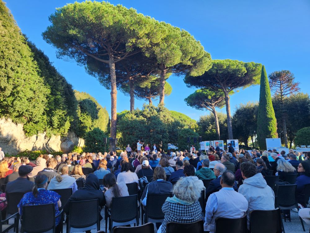 Crowd sits in chairs at outdoor conference.