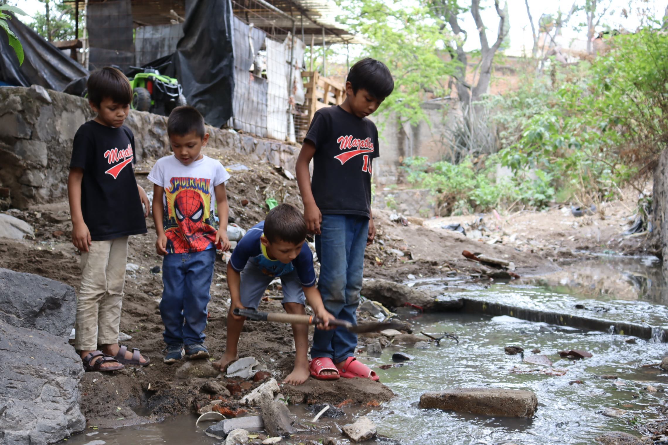 Mateo forma un camino en el riachuelo para que las hermanas Estrella Martínez y Monserrat Mendoza puedan cruzar durante su visita a la Colonia Villa de Guadalupe, Zapopan, México (Foto: Eduardo Cordero)