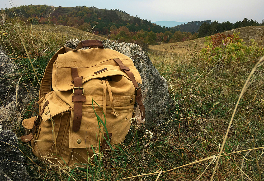 A brown backpack is seen against a grassy hill in this photo illustration. (Unsplash/Adam Hornyak)