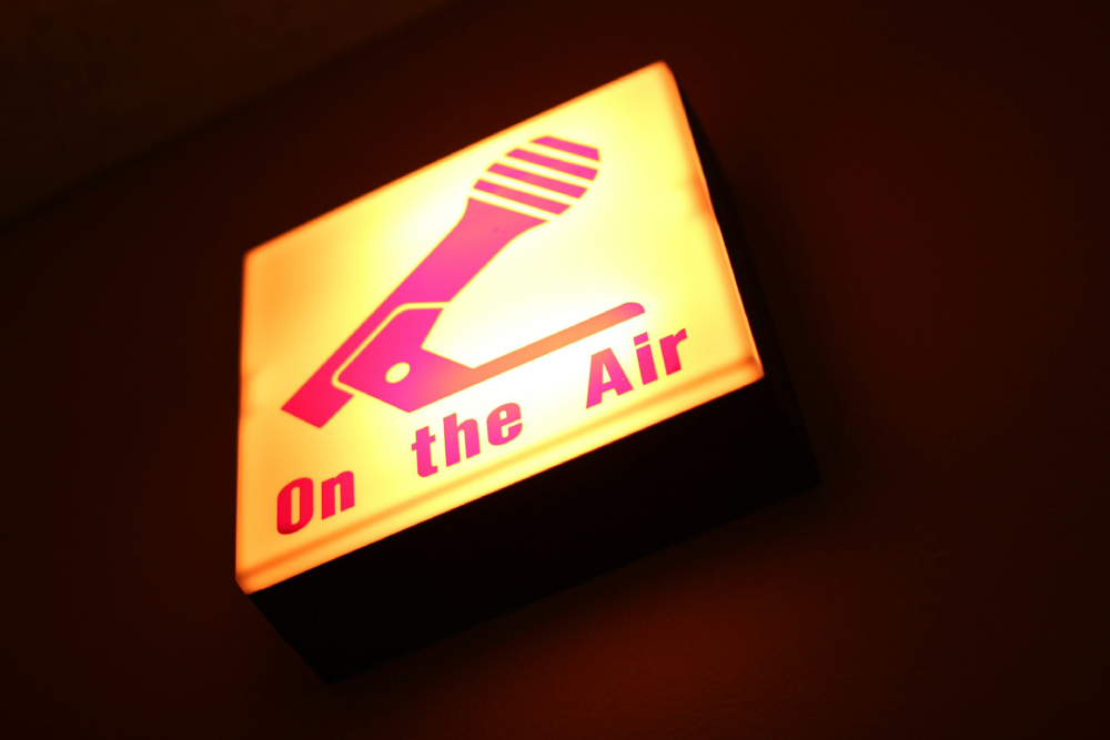 Bright yellow sign reads "On the Air" in red text with a red illustration of a microphone above it. 