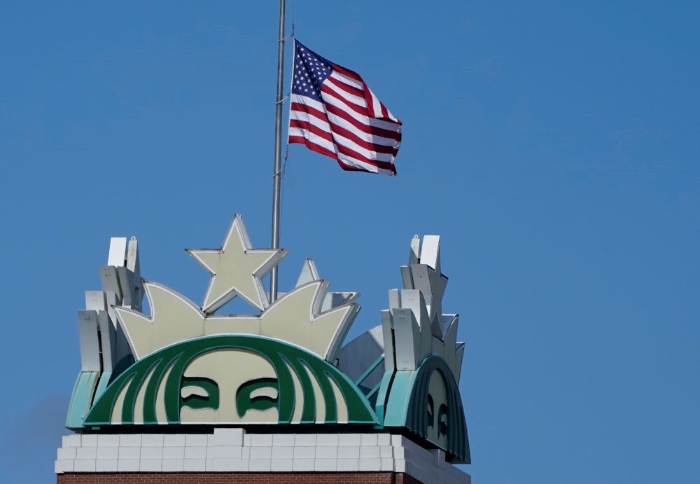 The U.S. flag flies above the Starbucks mermaid logo April 26, 2021, at the coffee company's corporate headquarters in Seattle. (AP/Ted S. Warren)