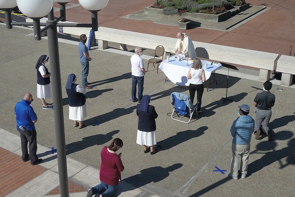 People standing outside socially distanced while a priest celebrates Mass