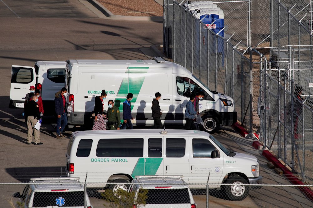 Migrants in the custody of the U.S. Border Patrol file into a Border Patrol station in El Paso, Texas, March 15, 2021. (CNS/Reuters/Paul Ratje) Vans from Border Patrol parked at a fence while people get out and walk