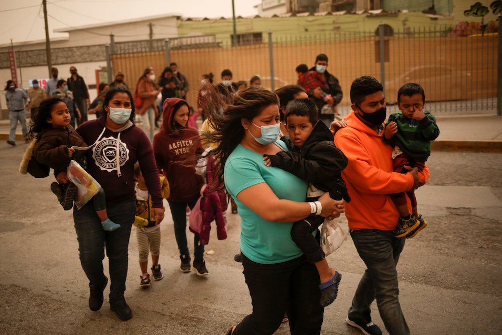 Asylum-seeking migrants from Central America who were airlifted from Brownsville, Texas, to El Paso, walk near the Paso del Norte international border bridge in Ciudad Juárez, Mexico, March 16, 2021. (CNS/Reuters/Jose Luis Gonzalez) People from Central America wearing masks and carrying children outside near the Paso del Norte international border bridge in Ciudad Juárez, Mexico