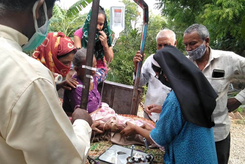 Fr. Ajeesh Chirayarikil, left foreground, helps Sr. Lisset Vadakkekara, at right in blue, administer an IV drip to a woman with COVID-19 symptoms in front of Jyoti clinic, managed by Congregation of Mother Carmel nuns at Chachana village in Gujarat, India