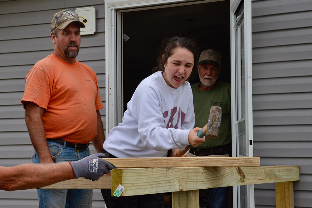 Volunteers Ronnie Mattingly, left, and Jude Leake watch as Lizzi Seyle, also a volunteer, tries the sledgehammer May 23 as the Sisters of Charity of Nazareth's disaster recovery team finishes building a porch on a home badly damaged by a Dec. 10 tornado.