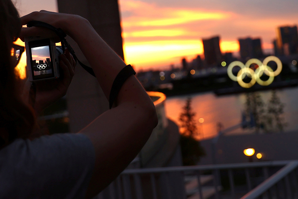 Olympics Japan A person photographs the Olympic Rings in front of the skyline during sunset July 20 in Tokyo, three days ahead of the official opening of the 2020 Olympic Games. (CNS/Reuters/Kai Pfaffenbach)