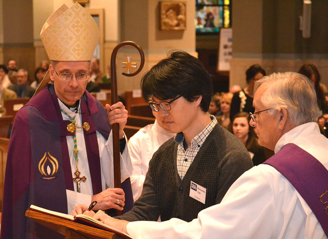 Bishop Mark L. Bartchak of Altoona-Johnstown, Pa., looks on as catechumen Dooyoung Lim signs his book of elect Feb. 22 at the Cathedral of the Blessed Sacrament in Altoona-Johnstown. (CNSMsgr. Tim Stein, Catholic Register)
