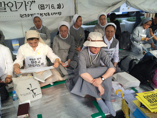 Women religious sit Tuesday with families of those who died in the April 16 sinking of a ferry to show support for an independent investigation of the disaster. The families have been protesting in the Seoul, South Korea, plaza where Pope Francis is to beatify 124 martyrs for 30 days. (NCR Photo/Thomas C. Fox)