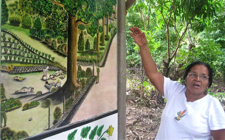 Maria Rosario Lopez Sanchez explains memorial mural outside a chapel in La Joya, one of the El Mozote area massacre sites. Sanchez testified at the Inter-American Court of Human Rights session that resulted in the El Mozote decision.