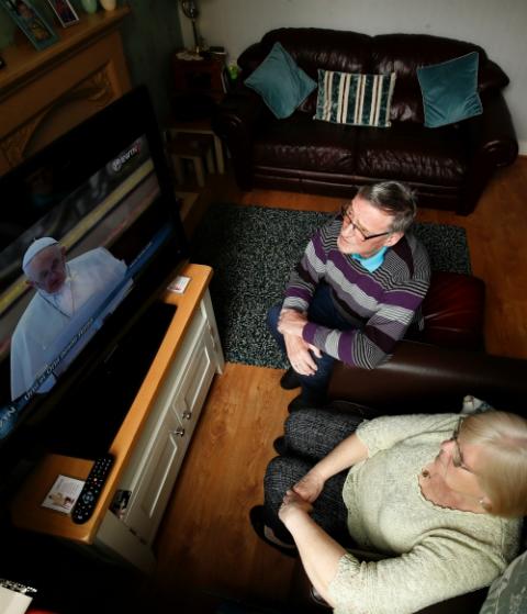 A couple watches Pope Francis from their home in Belfast, Northern Ireland, as he celebrates Easter Mass April 12 in St. Peter's Basilica at the Vatican. (CNS/Reuters/Jason Cairnduff)