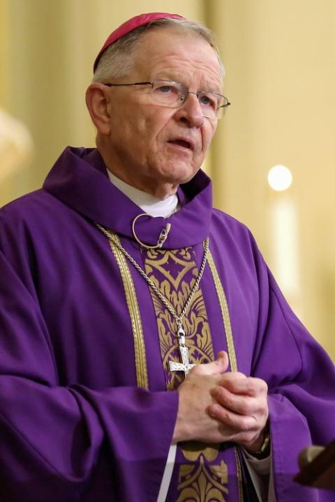 Archbishop, vested in purple, folds hands while preaching. 